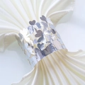 Detailed view of silver hollow clover napkin ring on white satin fabric - Reflective Silver