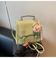 Detail der hellgrünen Handtasche mit Krokostruktur, Metallschnalle und Plüschbär-Anhänger - Grün mit Anhänger