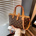 Braune Monogramm-Beuteltasche mit goldenen Beschlägen und Tragegriff im warmen Licht - Braun
