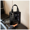 Close-up of black patent leather handbag featuring silver logo and heart charm detail - Black