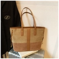Détail d'un grand sac cabas tissé avec poignées en cuir marron sur une valise argentée - Marron