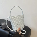 Light blue quilted bucket bag with silver studs and chain strap shown on black cushion - Blue