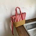 Detailed side view of red striped canvas and woven straw tote bag on wooden surface - Red