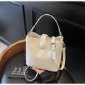 White woven bucket bag with elegant texture and adjustable shoulder strap on wooden chair - Off-white