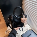 Glossy black bucket bag with a top circular handle and a plush bear charm - Black