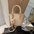 Creamy white bucket bag with pebble leather and cute bear charm in warm lighting - Beige With Charm