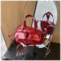 Detail of dark red patent leather handbag featuring glossy finish and decorative bow ties - Red