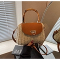 Detail showing hand holding woven straw bag with bamboo handle and brown leather flap - Off White
