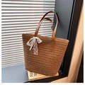 Close-up of woven straw tote bag with white lace bow and brown leather handles - Brown