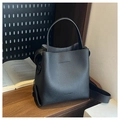 Detail of black lychee leather bucket bag with wide strap on a rustic wooden table - Black