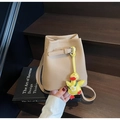 Chic beige lychee leather bucket bag with a cute yellow duck pendant on dark wood stairs - With Charm / Khaki