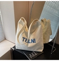 Detail van minimalistische crèmekleurige canvas tas met blauw TFLN! borduursel erop - Broken Wit