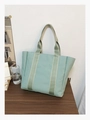 Close-up of mint green canvas tote bag with striped straps on a dark wood table - Green