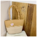 Detail of woven straw tote bag featuring two-tone color block and purple flower charm - Khaki