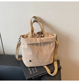 Close-up of beige canvas bucket bag with drawstring closure and metal logo on leather stool - Khaki