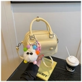 Gros plan d'un sac à main jaune crème avec pompon monstre dans un café chic - Avec Pendentif / Jaune