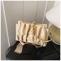 Detail van beige geplooide schoudertas met geweven handvat en glanzende afwerking op boek - Broken Wit