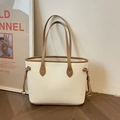 Minimalist beige tote bag with brown handles and gold hardware in a modern room setting - Off White