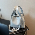 Lichtgrijze bucket bag met krokodillenprint, handvat en schouderband op een boek - Blauw