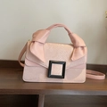 Pink snakeskin pattern crossbody bag with a large black buckle on a wooden stand - Pink