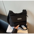 Detail of a black nylon crossbody bag featuring a front flap pocket and a branded rubber logo - Black