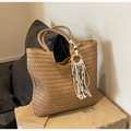 Brown woven straw tote bag with evil eye tassel charm on a neutral pedestal - Khaki