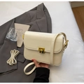 Sac bandoulière en cuir verni crème avec fermoir doré sur une veste grise - Beige