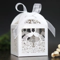White laser-cut peacock wedding candy box with elegant silk ribbon bow on wood surface - White