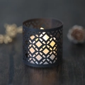 Close-up of black laser-cut geometric hollow candle holder with warm yellow light - Black