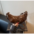 Close-up of vintage dark brown patent leather dumpling bag with decorative knot and gold hardware - Coffee