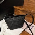 Borsa a secchiello nera intrecciata con tracolla regolabile su sfondo di scale in legno - Nero