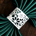 Detailed laser-cut white floral paper napkin ring on a dark green satin napkin - White