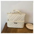 Detailed view of cream quilted tote bag with diamond pattern and metal logo on wood surface - Off White