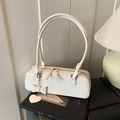 Cream white baguette bag with dual handles and heart charm in a warm lifestyle setting - White