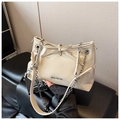 Close-up of beige glossy handbag featuring a large bow detail and gold metal chain strap - Khaki
