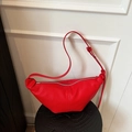 Red lychee leather croissant shoulder bag with knotted strap on black wooden stool - Red