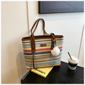 Detail of colorful striped woven tote bag with brown leather handles and leaf charm - Colorful
