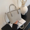 Grey textured leather bucket bag with top handles and fashion text detail on white surface - Gray