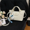 Creamy white lychee texture mini tote bag with cute plush rabbit charm on black sofa - Beige With Charm