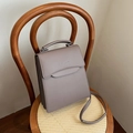 Elegante bolso bandolera color topo con asa curva sobre una silla de ratán en interior - Caqui