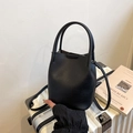 Minimalist black pebbled leather bucket bag with dual handles on a white suitcase - Black