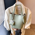 Sage green leather bucket bag with silver chain charm shown with a commuter suit - Green