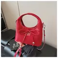 Close-up of a bright red patent leather handbag with bow detail and silver chain strap - Red