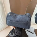Blue denim crossbody pillow bag with silver zipper and adjustable strap shown by hand - Dark Blue