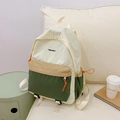 Detailed view of color-block nylon backpack featuring orange zipper pulls on fabric sofa - Green