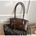 Detail of dark brown tote bag with woven knot and golden tennis racket charm in soft light - With Charm / Brown
