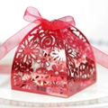 Close-up of laser-cut red wedding favor box with intricate floral hollow patterns and ribbon - Double Sided Reflective Red