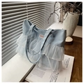 Dettaglio borsa tote in denim azzurro con balze in rete bianca e etichetta decorativa moda - Azzurro