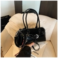 Detail view of black glossy leather handbag with long handles on light fabric background - With Pendant Style / Black