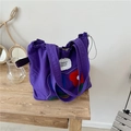 Purple canvas tote bag with red flower patch and drawstring closure on a wooden desk - Purple